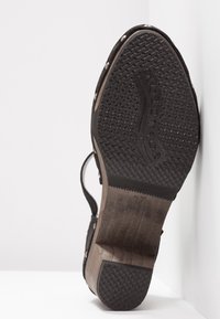 Sandale noire avec une semelle en caoutchouc texturé, un talon en bois et des clous décoratifs le long du bord. Taille 37 marquée sur la semelle.