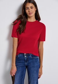 Röd kortärmad t-shirt i slät tyg, rundad halsringning, figurnära passform, kombinerad med blå denimjeans. Enkel, stilren design.