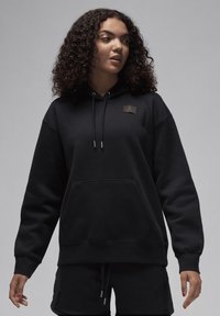 Sweatshirt com capuz preto feito de tecido macio, apresentando um bolso frontal, cordões e um patch de logotipo texturizado no lado esquerdo do peito.