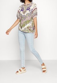 Lätt, blommönstrad blus med puffärmar, i kombination med ljusblå skinny jeans och beiga slide-sandaler.