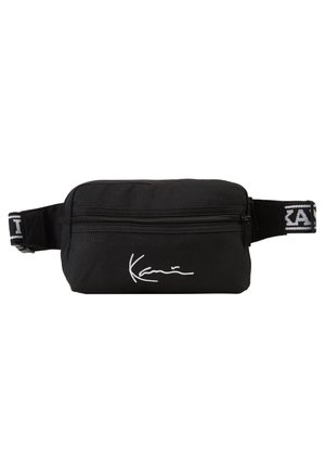 Black fanny pack made of durable fabric, featuring a zippered compartment, adjustable strap, and white signature logo on the front.
