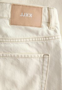 Τζιν τζιν σε κρεμ χρώμα με πίσω τσέπη με καφέ δερμάτινη ετικέτα με την ένδειξη «JJXX» και ορατή θηλιά ζώνης και ραφές.