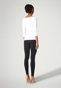 Weißes Langarmshirt mit Bootsausschnitt, kombiniert mit schwarzen Leggings und nudefarbenen High Heels. Glatter Stoff und taillierter Schnitt betonen die Silhouette.
