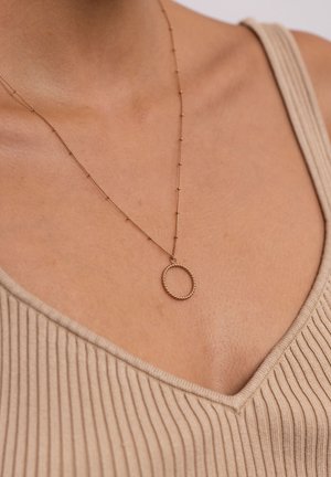 Goldfarbene Halskette mit einem ovalen Anhänger, der einen strukturierten Rand aufweist, und von einer zarten Kette mit kleinen Perlenakzenten gehalten wird.