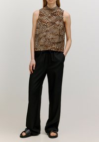 Ärmelloses Oberteil mit Leopardenmuster und hohem Kragen, kombiniert mit lockeren schwarzen Hosen und schwarzen Sandalen. Glattes Material und lässige Passform.