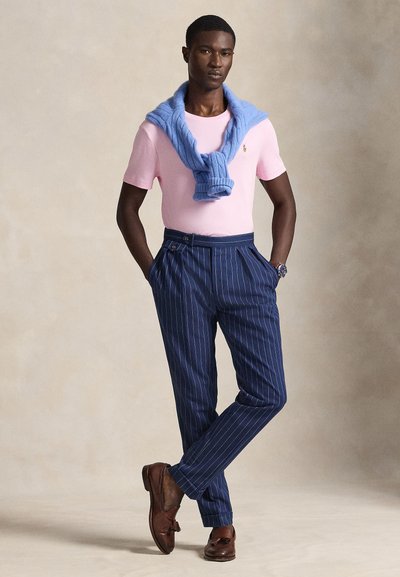 Šviesiai rožinė marškinėliai, melsvas megztinis apsivilktas aplink kaklą, tamsiai mėlynos pinstriped kelnės ir rudi odiniai batai. Klasikinio, pritaikyto silueto.