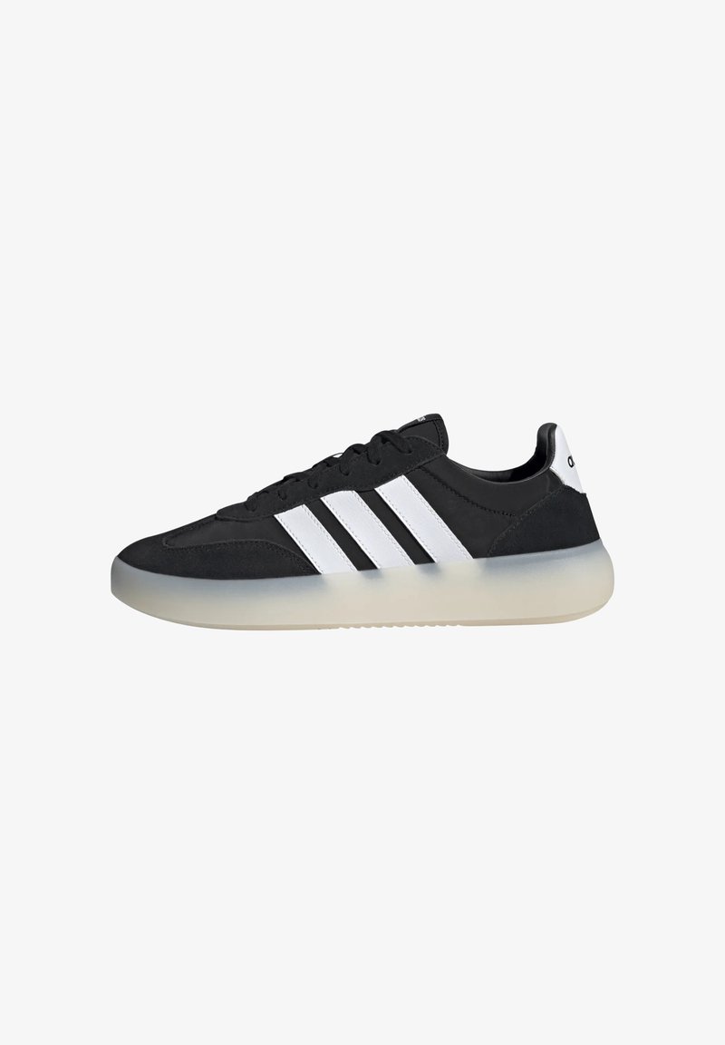 Sneaker nera con una texture liscia, tre strisce bianche e una suola semi-trasparente. Punta arrotondata e design con lacci.