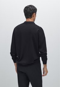 Schwarzes Longsleeve-Polohemd mit einem schlichten Kragen, das eine lockere Passform und gerippte Bündchen sowie Saum aufweist. Das Material wirkt weich und glatt.