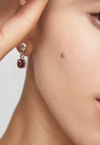 Pendientes de plata con un botón redondo y una piedra preciosa cuadrada violeta colgante, que muestran una textura suave y un acabado pulido.