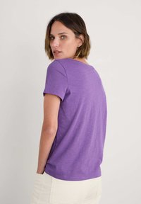 Camiseta corta de manga corta en color púrpura con un corte relajado y un escote redondeado, que presenta una textura suave y ligera, y un estilo casual.