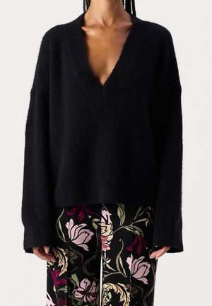 Pull noir duveteux à col en V avec manches longues, associé à un pantalon noir présentant de grands motifs floraux roses, rouges et verts.