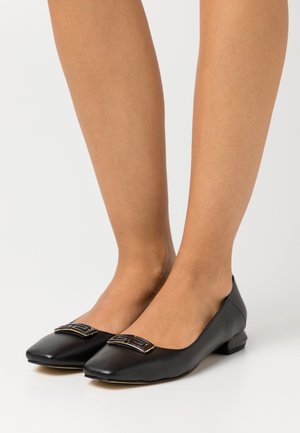 Černé kožené baleríny s kulatou, nízkou patou. Mají obdélníkovou sponu se zlatým akcentem na špičce a hladký povrch.