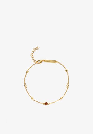 Złota bransoletka z łańcuszkiem, ozdobiona okrągłymi czerwonymi i przezroczystymi kamieniami, wyposażona w zapięcie typu karabińczyk oraz regulowany łańcuszek umożliwiający dostosowanie rozmiaru.