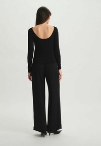 Haut noir à manches longues avec un dos décolleté, associé à un pantalon noir fluide. Sa texture lisse et sa coupe décontractée créent une silhouette minimaliste.