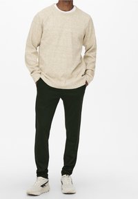 Beige textured sweatshirt with a round neck, paired with dark green tapered pants and light sneakers with black accents.