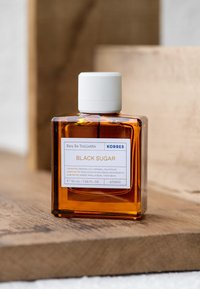 Eau de Toilette by Korres in a clear glass square bottle, amber liquid, white screw cap, featuring a label with scent notes and brand name.