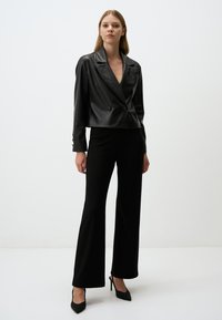 Zwart leren cropped jack met dubbele knopen, piekkleppen en lange mouwen. Gecombineerd met zwarte hoge taille flared broeken en hoge hakken.