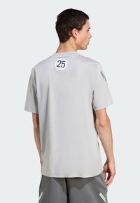 Lys grå t-shirt med korte ærmer, der har et cirkulært sort "25" på ryggen og en glat, blød tekstur. Enkel design.