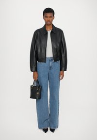 Veste en cuir noire courte sur un haut gris clair, associée à un jean ample bleu taille haute et un petit sac à main noir.