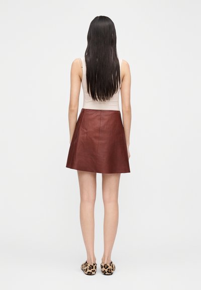 Rudos odos sijonas su plataus silueto dizainu, lygiu paviršiumi ir minimaliais siūlių akcentais. Dėvimas su kreminės spalvos palaidine ir leopardo rašto šlepetėmis.