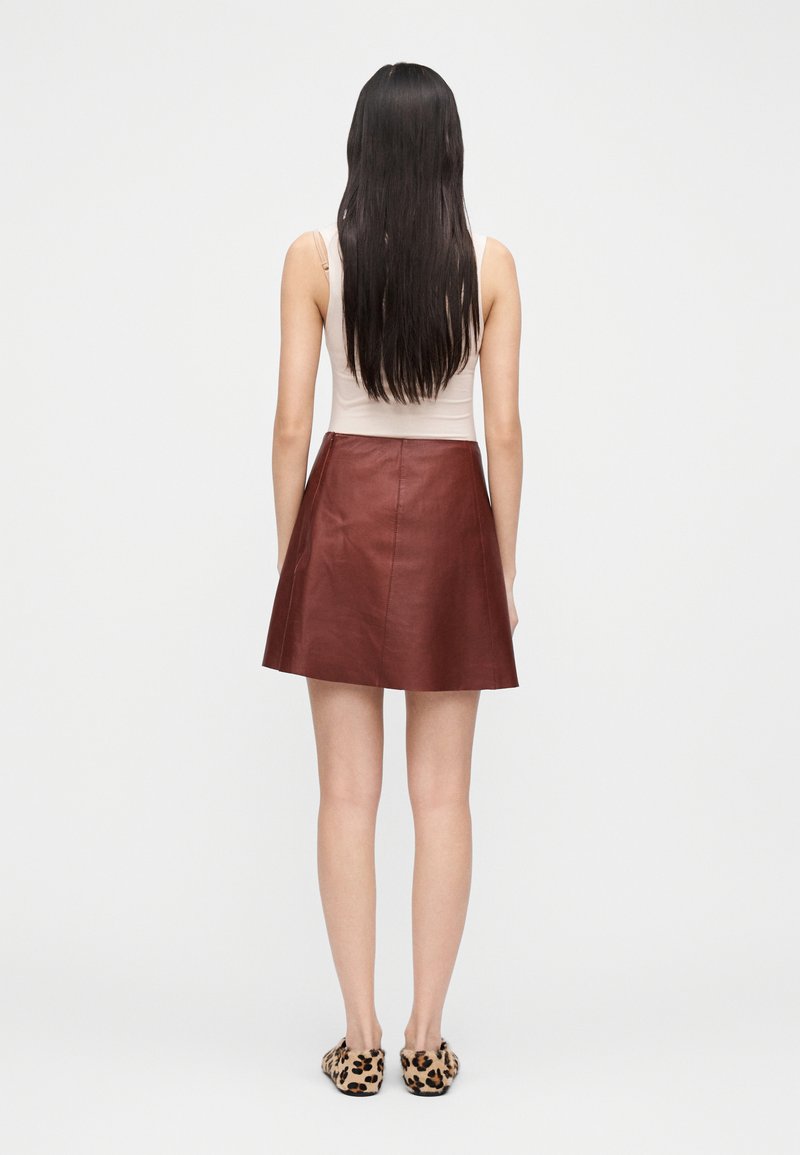 Brun lædernederdel med en udvidet pasform, glat struktur og minimal syning. Bæres med en beige top og leopardmønstrede tøfler.