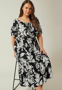 Vestido negro con estampado floral blanco, diseño sin hombros, mangas abullonadas y cintura ceñida. Dobladillo en capas y tela liviana.