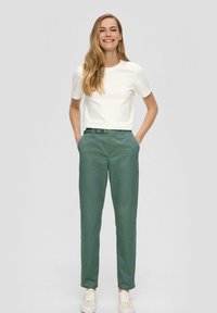 Weißes T-Shirt mit kurzen Ärmeln, grüne Hose und helle Sneakers. Die Hose hat einen Gurtbund, eine glatte Textur und einen geraden Schnitt.