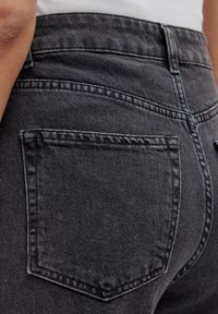 Zwarte denim jeans tonen een close-up van de achterzak, met een matte textuur, contrasterende stiksels en een hoogtaille ontwerp.