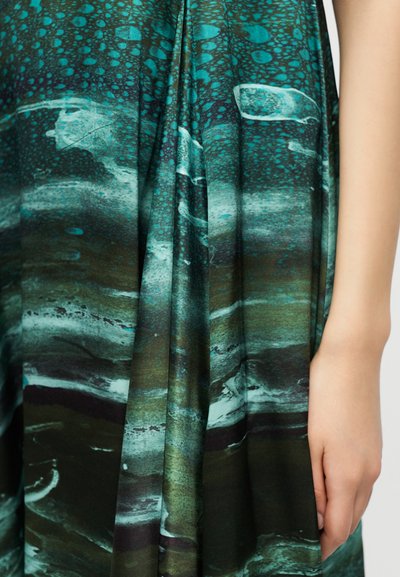 Ρευστή υφή με τυρκουάζ και πράσινο αφηρημένο, μαρμάρινο μοτίβο που κρέμεται δίπλα σε χαλαρό χέρι και βραχίονα.