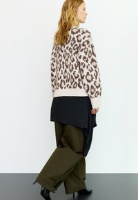 Bézs és barna leopárdmintás kötött pulóver fekete ing fölött, olívazöld, bő szárú nadrággal és fekete magassarkú csizmával párosítva.
