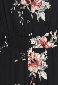 Svart tyg med blommönster i rosa och vita blommor. Knappslå fram, gathering-textur vid midjan.