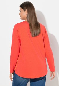 Rotes Langarmshirt mit abgerundetem Saum und Seitenschlitzen, hergestellt aus leichtem Stoff. Bietet eine lockere Passform und ein schlichtes Design.
