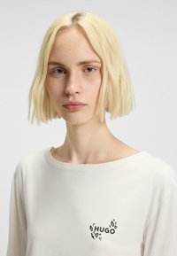 Witte lange mouwen shirt met een zwart "HUGO" logo met luipaardprintaccenten op de linkerkant van de borst. Gladde stof en een ontspannen halslijn.
