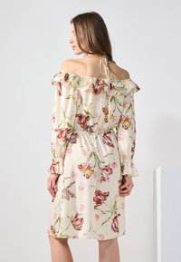 Robe fleurie à épaules dénudées avec un col froncé, tissu crème, motifs de fleurs roses et rouges, taille élastique et longues manches avec des poignets froncés.