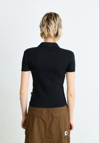 Svart polo skjorta med korta ärmar och klassisk krage, tillverkad av strukturerad tyg, tillsammans med en brun funktionell kjol med fickor.