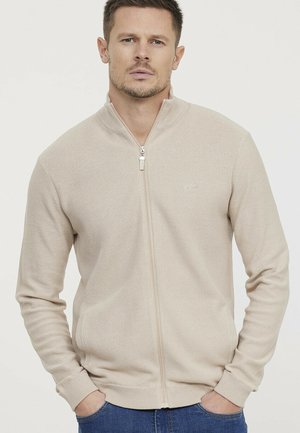 Beige zip-up sweater with a textured finish, long sleeves, and ribbed cuffs. Features a stand-up collar and side pockets. Casual design.