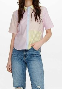 Chemise à col à manches courtes présentant un design à rayures pastel, avec des sections en rose, jaune et bleu clair, associée à un short en denim déchiré.