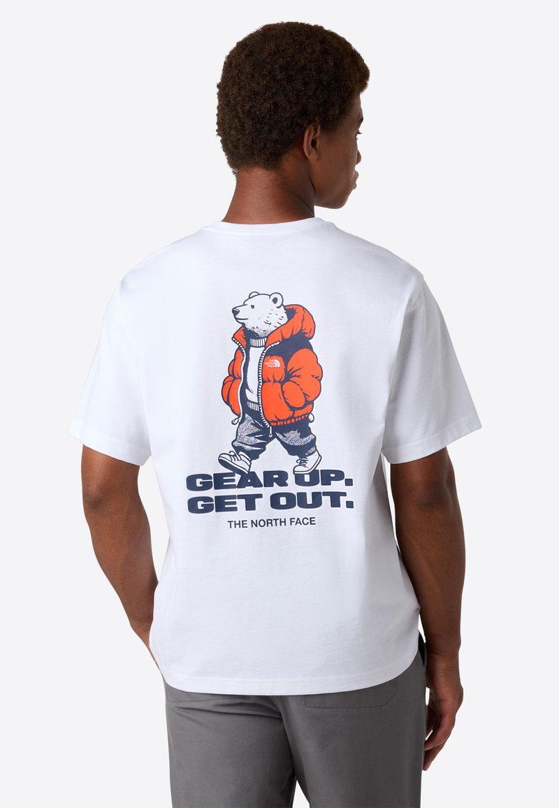 Mand i hvid T-shirt med grafik af en bjørn i orange jakke og grå bukser, der går ved siden af teksten "GØR DIG KLAR. KOM UD. THE NORTH FACE" på ryggen.