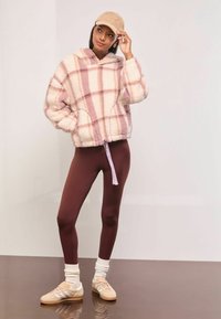 Rózsaszín és krém színű kockás bolyhos kapucnis pulóver, zsinórral a szegélyén, burgundi leggingsszel és krém színű zoknival párosítva, bézs cipővel kiegészítve.