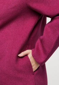 Indumento in fleece di un vibrante magenta con una vestibilità rilassata, dotato di una tasca laterale e maniche arrotondate per il massimo comfort. Texture morbida in tutto il capo.