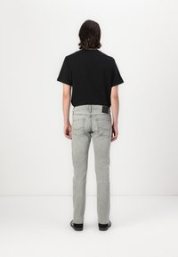 Grå slim-fit jeans med detaljer på baklommen, kombinert med en enkel svart t-skjorte, sett bakfra. Svarte sko fullfører antrekket.