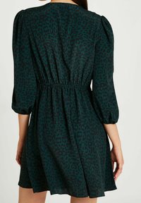 Vestido en azul oscuro con un patrón de leopardo, mangas abullonadas, cintura elástica y dobladillo acampanado. Tejido suave con una textura lisa.