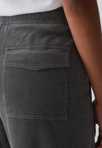 Pantalon en velours côtelé gris à rayures verticales, avec une poche arrière et un tissu texturé. La ceinture est élastique pour plus de confort.
