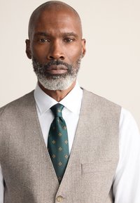 Gray houndstooth vest over a white dress shirt, paired with a dark green tie featuring a gold geometric pattern.