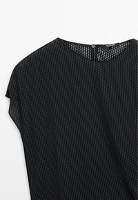 Czarny top z krótkimi rękawami i subtelnym pionowym wzorem krzyżowym, z okrągłym dekoltem i pojedynczym zapięciem na guzik z tyłu.