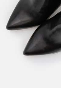 Tacones negros de cuero con punta afilada, con una textura suave y un acabado brillante, que presentan un diseño afilado para una silueta elegante.