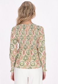 Langærmet bluse i mønstret stof med blomsterdesign i grøn, pink og creme. Smocket talje med en nøglehul detaille bagpå.