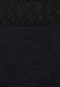 Pletená látka v tmavě černé barvě s texturovaným, šikmým vzorem rybí kosti v horní polovině a hladkým povrchem v dolní polovině.