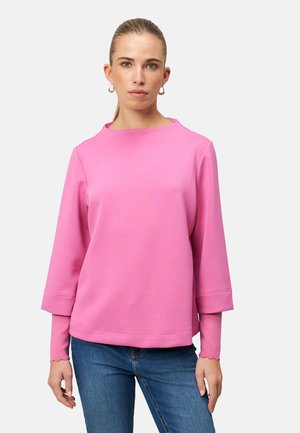 Pinker Sweatshirt mit rundem Ausschnitt und dreiviertel Ärmeln, ausgestattet mit gewellten Bündchen. Weiche Textur, kombiniert mit blauen Jeans.