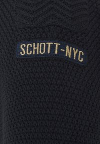 Svart stickad tröja med ett strukturerat mönster, med en blå broderad logotyp som läser "SCHOTT-NYC" i gyllene bokstäver.